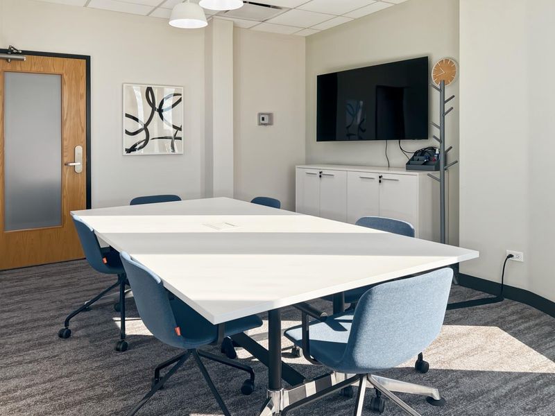 A professional office meeting room featuring a central table, built-in storage cabinetry, suspended ceiling tiles, and modern finishes.