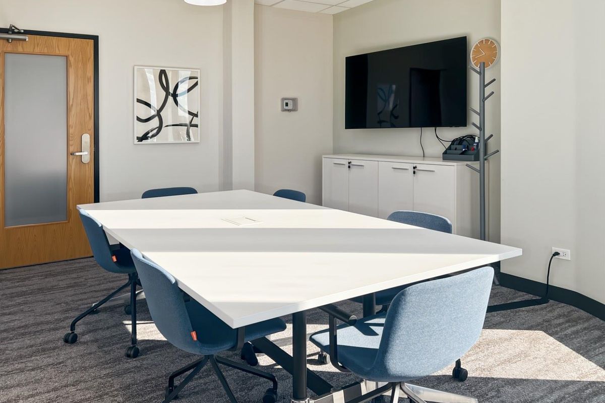 A professional office meeting room featuring a central table, built-in storage cabinetry, suspended ceiling tiles, and modern finishes.