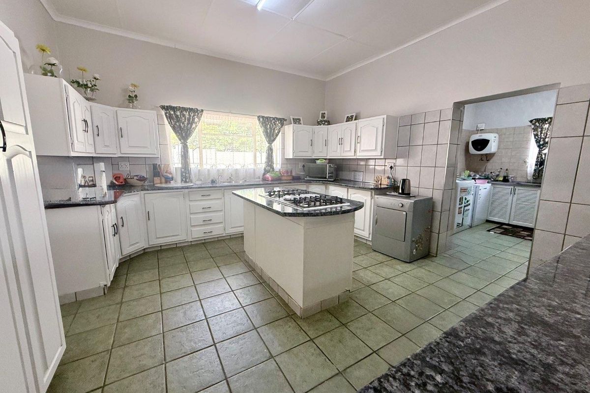 Spacious kitchen featuring white cabinetry, granite countertops, a central island with a built-in gas hob, and an adjoining scullery area.