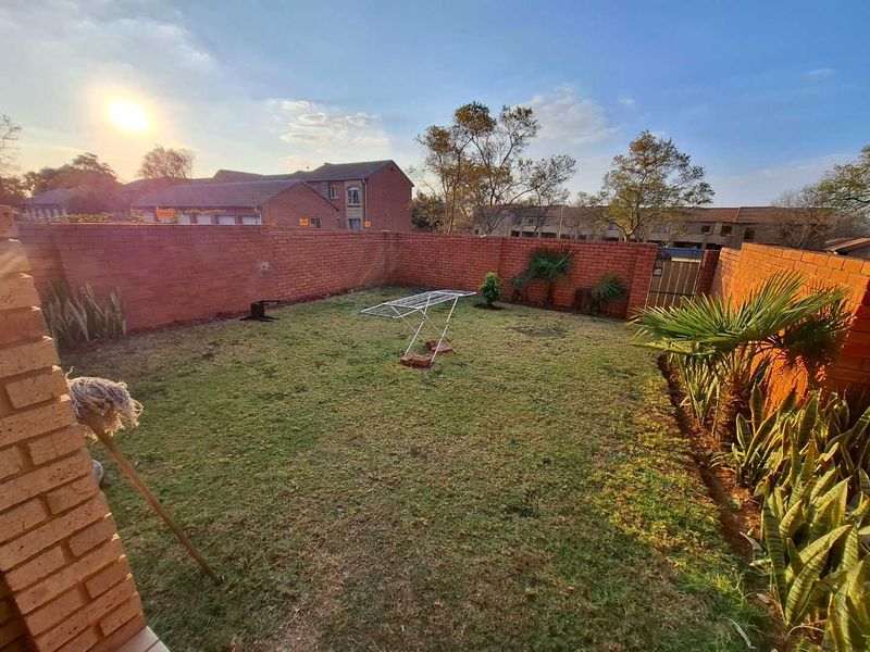 A private rear garden featuring a lawn area enclosed by brick boundary walls and a metal access gate.