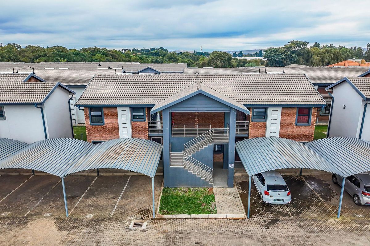 Aerial view of an apartment complex featuring brick facades, tiled roofs, and dedicated covered parking bays with paved driveways.