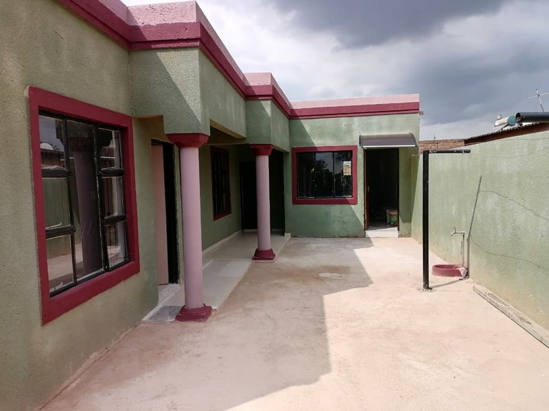 A rear exterior view of the house featuring a concrete patio area, structural columns, and external access points with aluminium window frames.