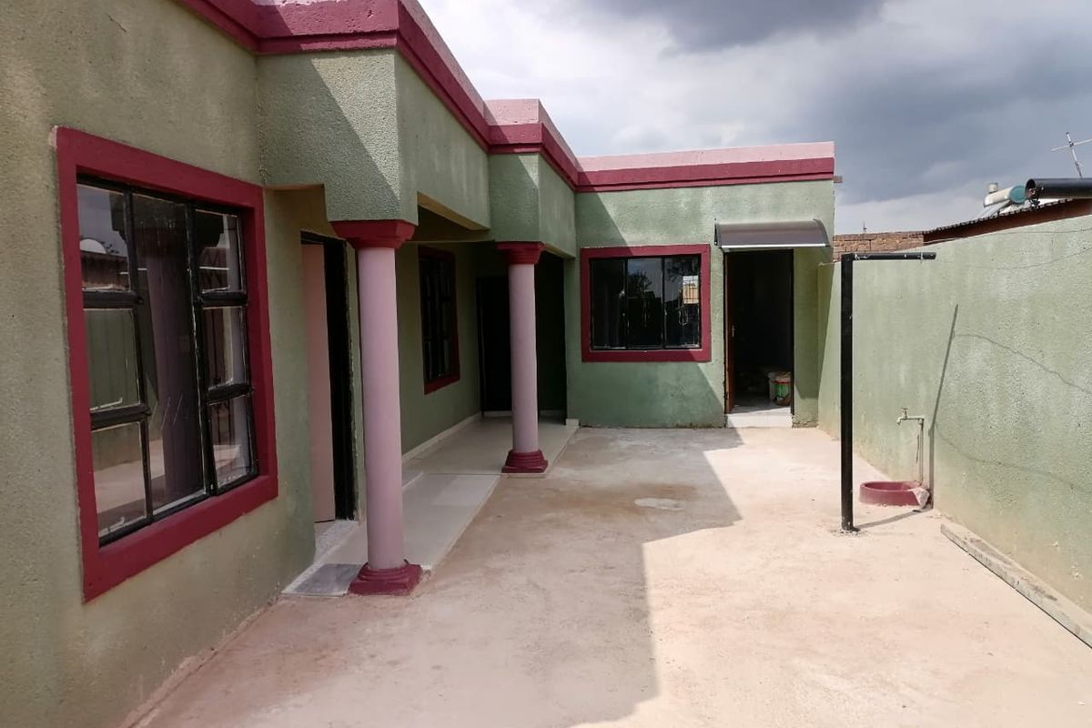 A rear exterior view of the house featuring a concrete patio area, structural columns, and external access points with aluminium window frames.