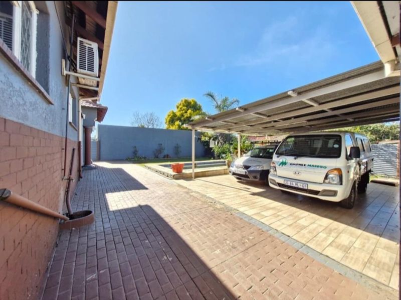 Rear exterior area featuring a paved driveway, covered carport, and a swimming pool.
