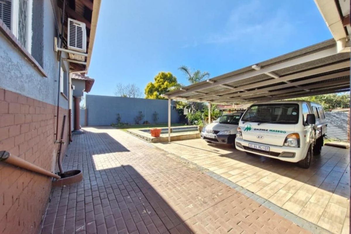 Rear exterior area featuring a paved driveway, covered carport, and a swimming pool.