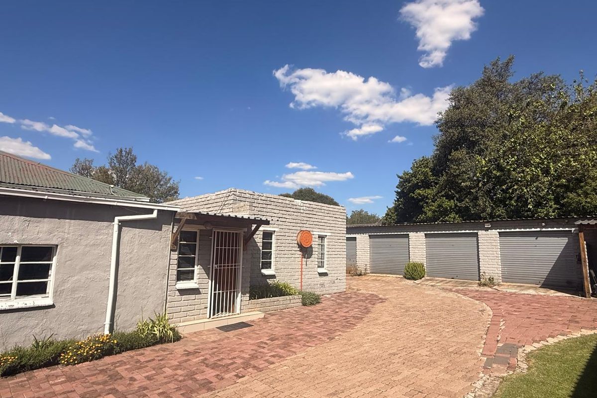 Exterior view of the property featuring a paved driveway, multiple garage units, and a brick-built structure with security gates.