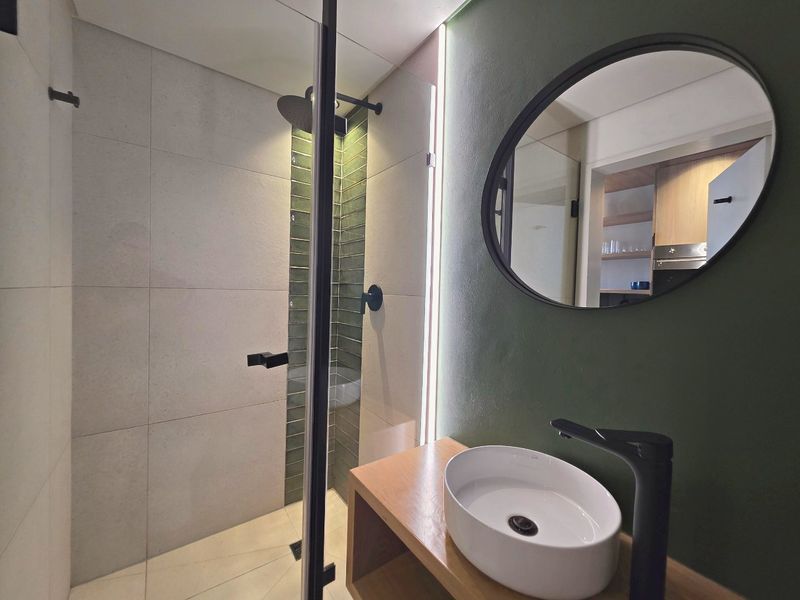 Modern bathroom featuring a walk-in shower with a rain shower head, a stylish vessel sink on a vanity unit, and elegant accent lighting.