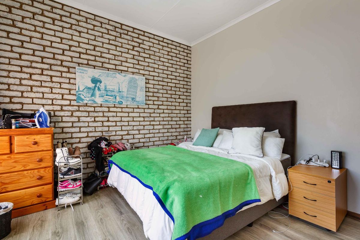 A bedroom featuring a distinctive exposed brick feature wall and modern wood-look flooring.