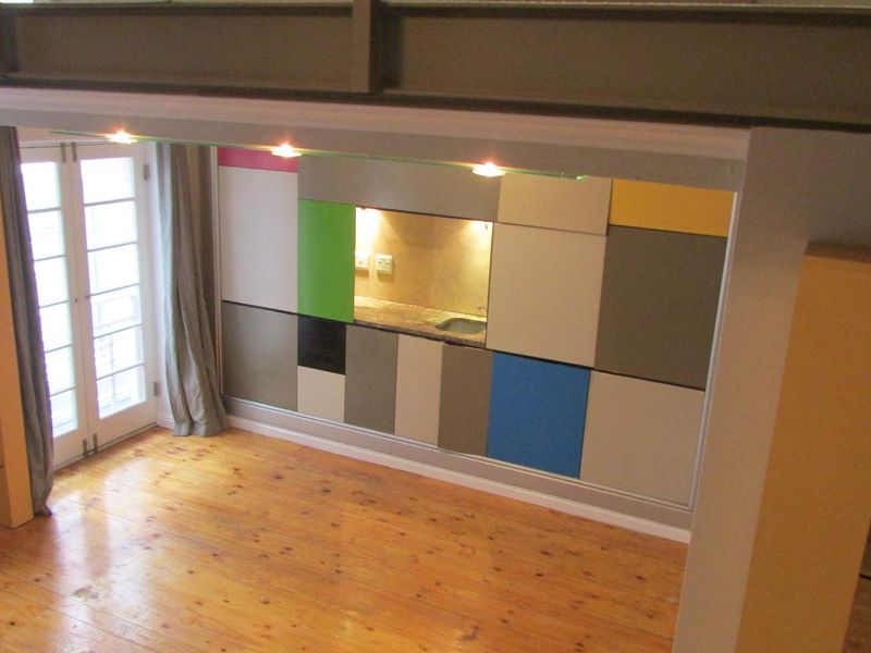Open plan living area featuring timber flooring, integrated kitchen cabinetry with a colorful geometric design, and direct access to a balcony through glass doors.