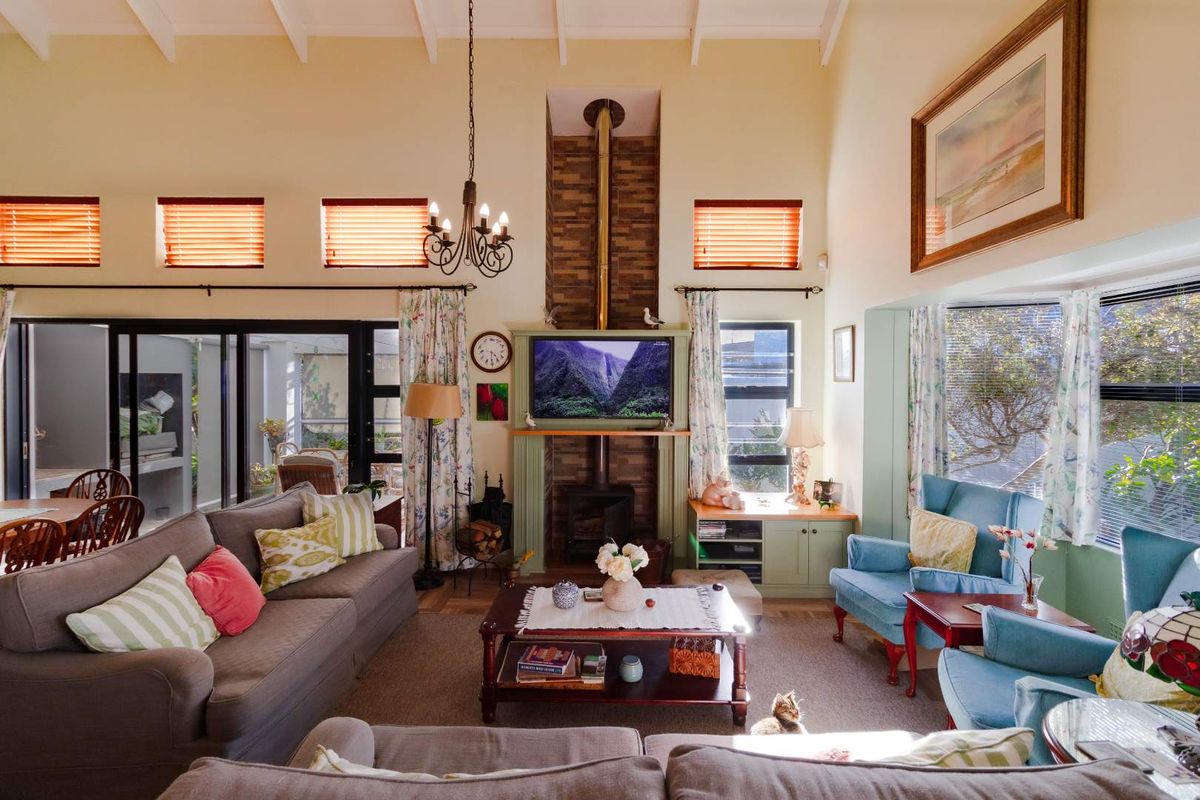 Spacious living room featuring a high vaulted ceiling with exposed beams, a central wood-burning fireplace with stone detailing, and large sliding doors to the patio.