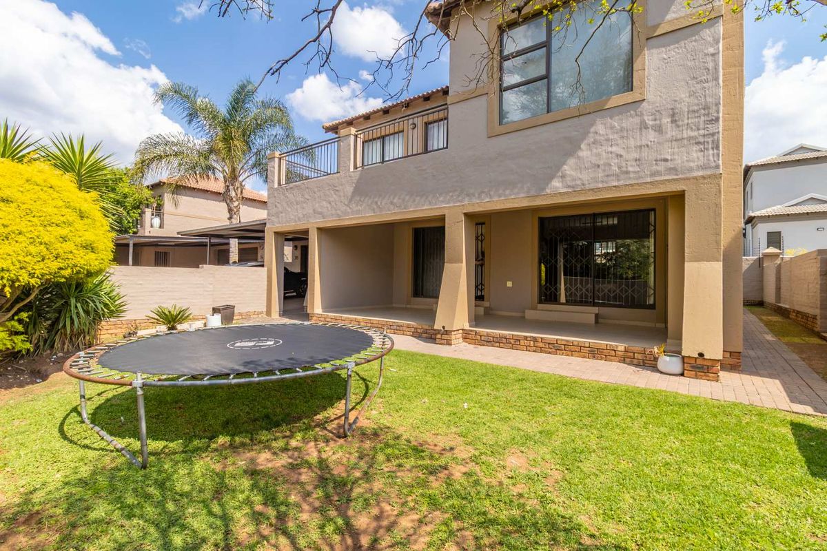 Rear view of the townhouse featuring a covered patio, an upper-level balcony, brick paving, and a private garden area.