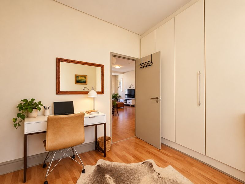 A well-maintained bedroom featuring light hardwood flooring and extensive built-in cupboard storage, with a view through to the adjacent living area.
