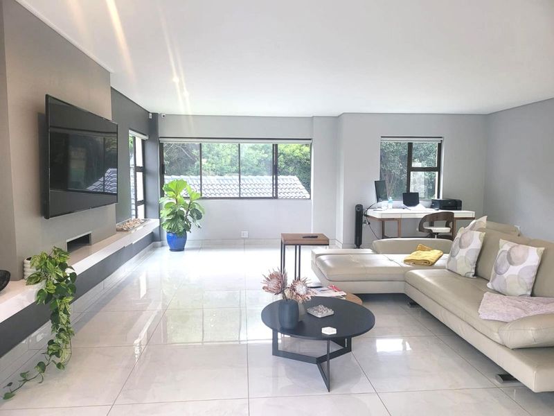 Spacious living room featuring large format floor tiles, a modern built-in media console, and ample natural light through aluminium-framed windows.