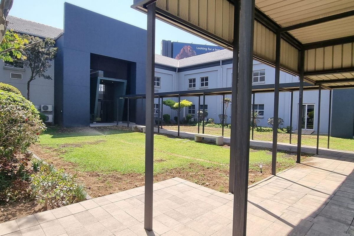 A view of the office building exterior featuring a central courtyard, paved walkways, and a covered metal pergola structure.