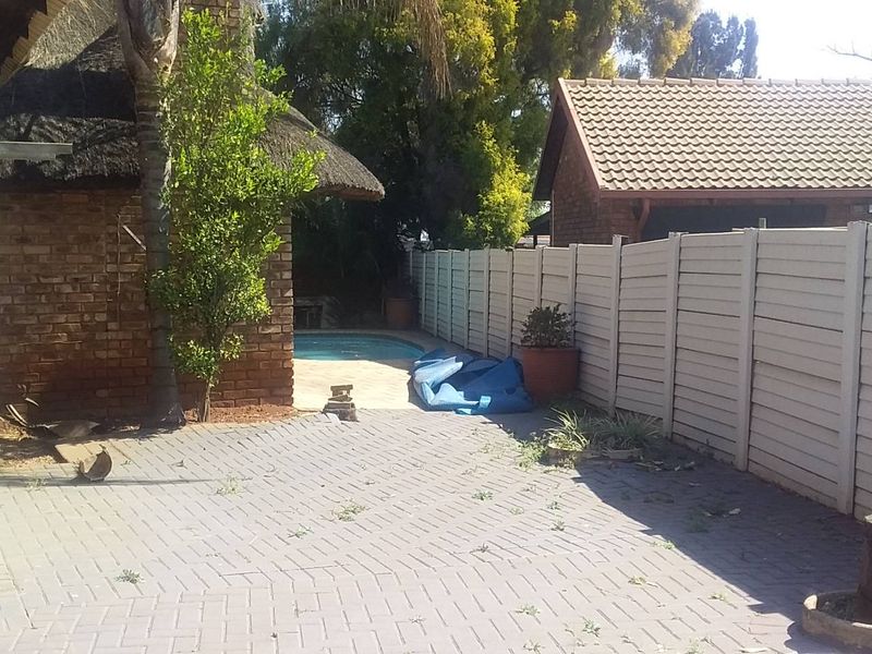 Rear exterior view featuring a brick house with a thatched roof, paved patio area, and a swimming pool enclosed by a precast concrete boundary wall.