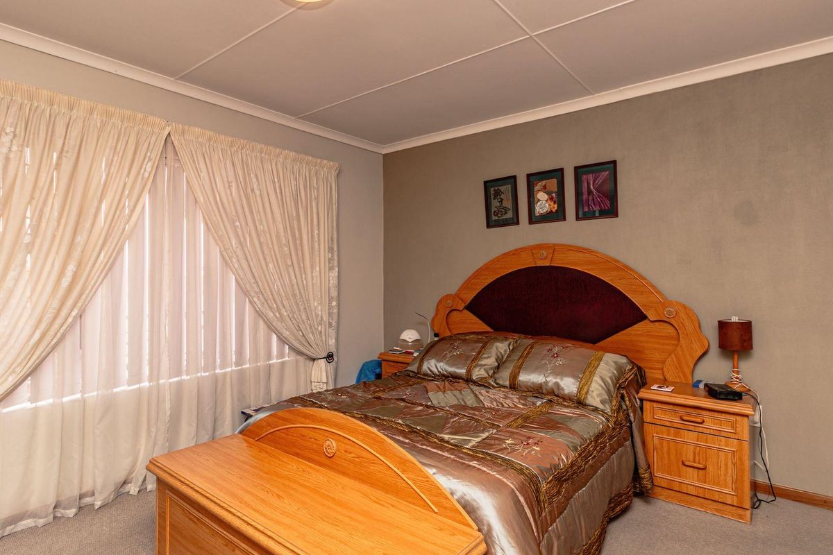 A standard bedroom featuring neutral wall tones, carpeted flooring, and a large window with curtain treatments.