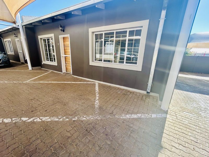 Front exterior view of the townhouse featuring a paved driveway, security gate, and well-maintained dark grey facade with white trim.