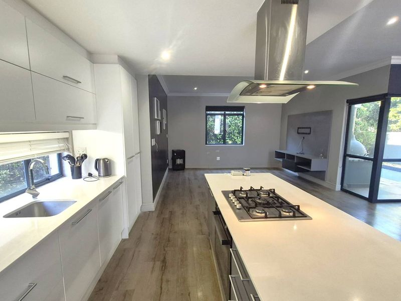 Modern open-plan kitchen and living area featuring a central island with gas hob, sleek white cabinetry, and contemporary finishes throughout.