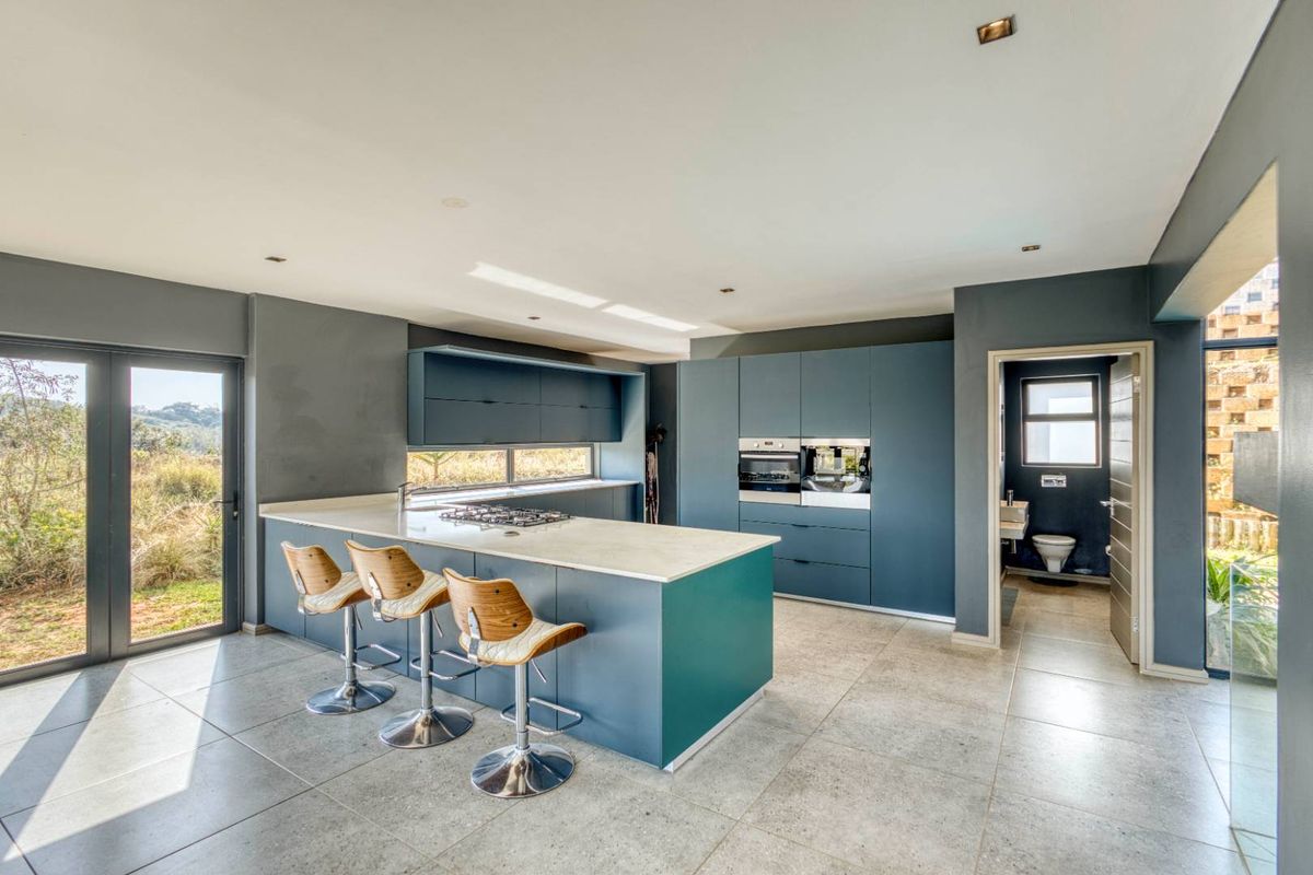 Modern open-plan kitchen featuring dark blue cabinetry, stone countertops, a central island with gas hob, and integrated appliances, with adjacent guest bathroom access.