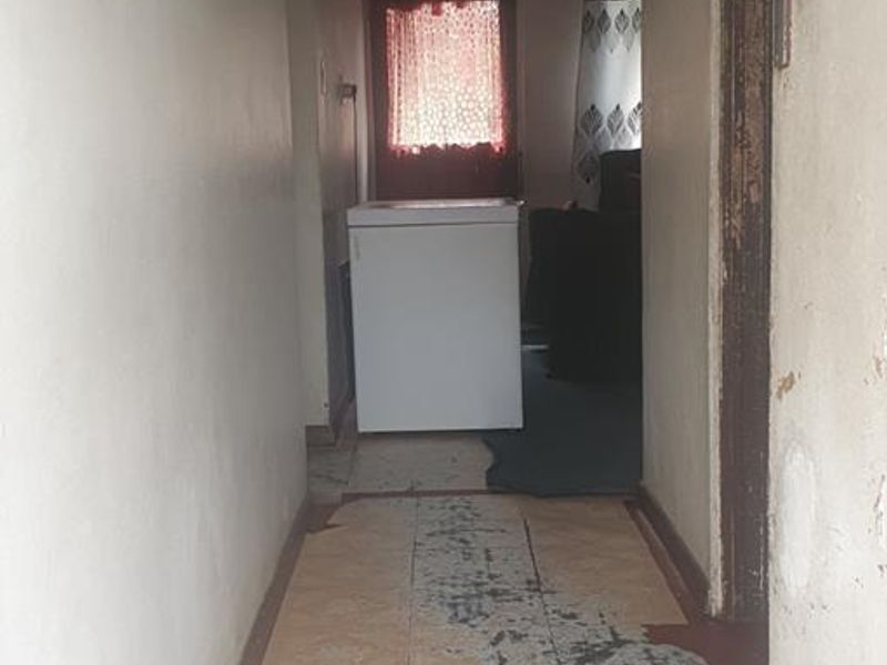A narrow interior hallway featuring worn tiled flooring and visible wear on the walls and door frames, leading towards an open living area.