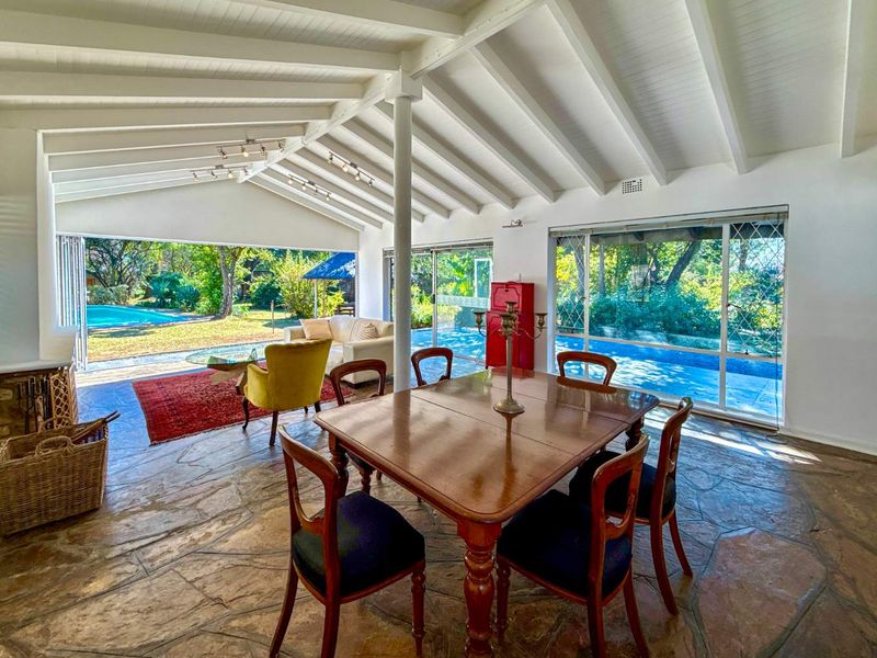 Spacious open-plan living and dining area featuring exposed beam ceilings, natural stone flooring, and large sliding doors opening to the pool and garden.