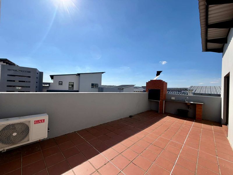 Spacious open-air balcony featuring a built-in braai, outdoor sink, and tiled flooring, offering a functional space for outdoor entertaining.