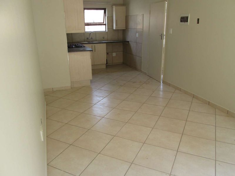 An empty open-plan kitchen and living area featuring tiled flooring, built-in cabinetry, and a gas hob, requiring minor cosmetic updates.