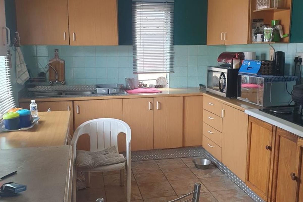A functional kitchen featuring light wood-finish cabinetry, tiled splashbacks, and tiled flooring, offering a practical layout with ample storage space.