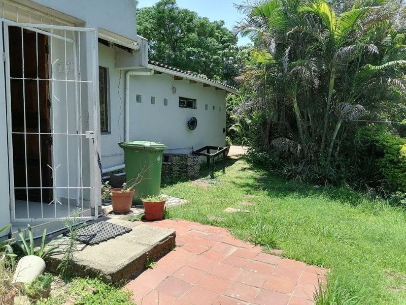 Rear exterior view of the apartment featuring a small terracotta paved area, security gate, and access to the garden space.