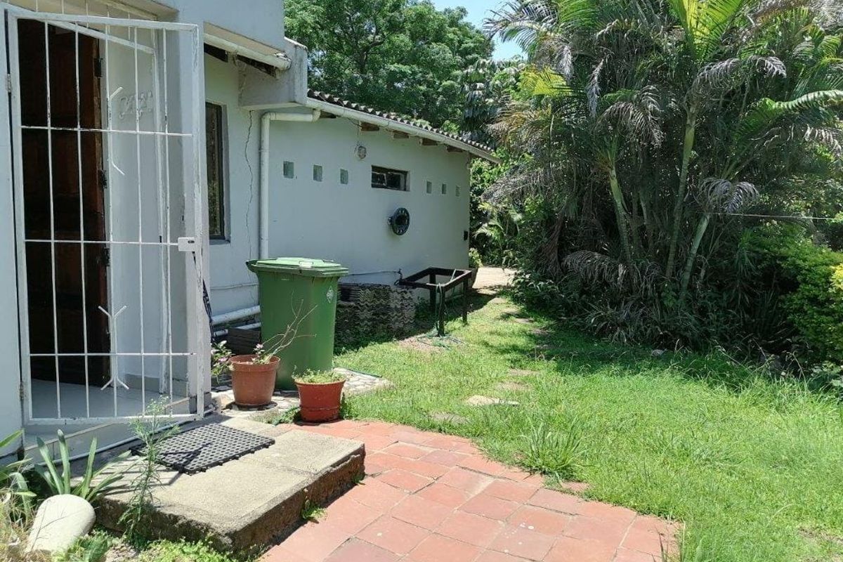 Rear exterior view of the apartment featuring a small terracotta paved area, security gate, and access to the garden space.