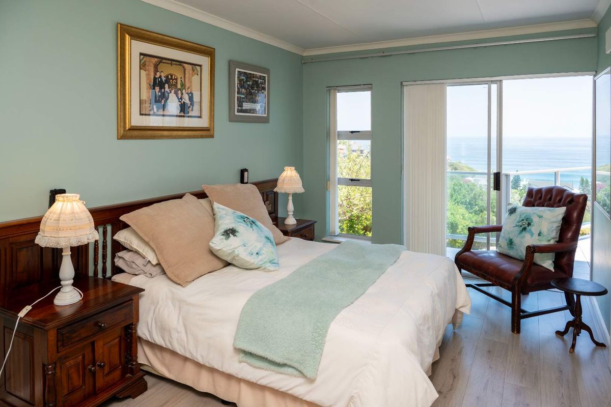 A well-lit bedroom featuring light wood-look flooring, sliding glass doors leading to a balcony, and expansive ocean views.