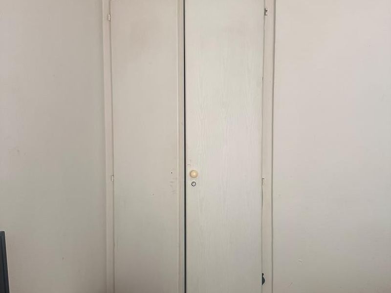 A bedroom featuring a built-in wardrobe with white folding doors, coving, and timber flooring.