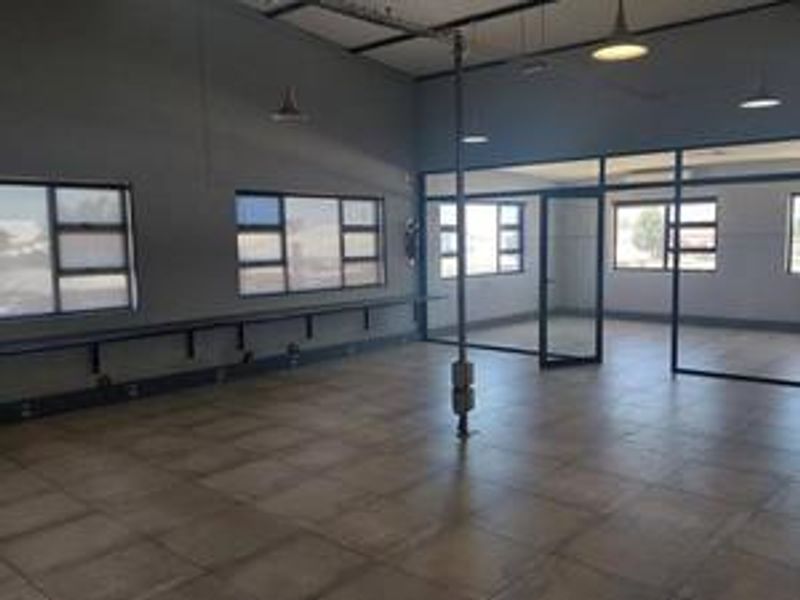 Spacious industrial office area featuring tiled flooring, large windows, and modern glass partitions, providing a clean and professional workspace environment.
