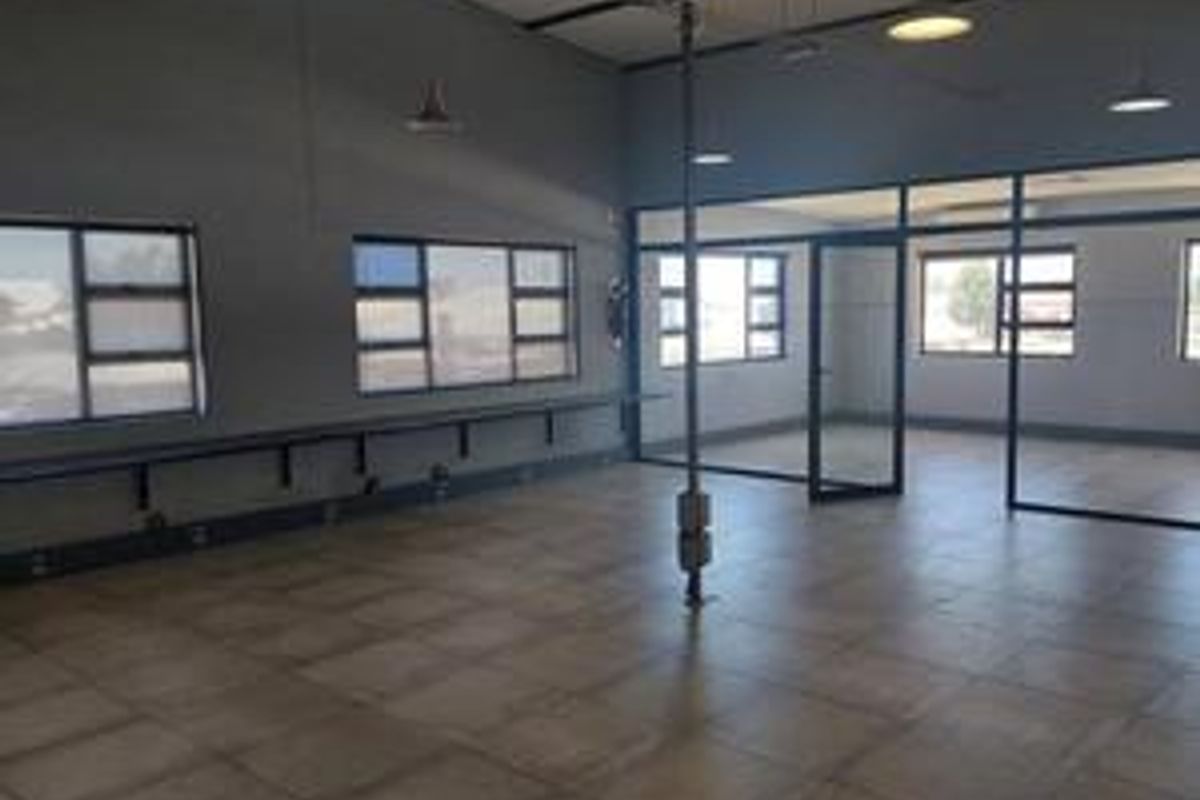 Spacious industrial office area featuring tiled flooring, large windows, and modern glass partitions, providing a clean and professional workspace environment.