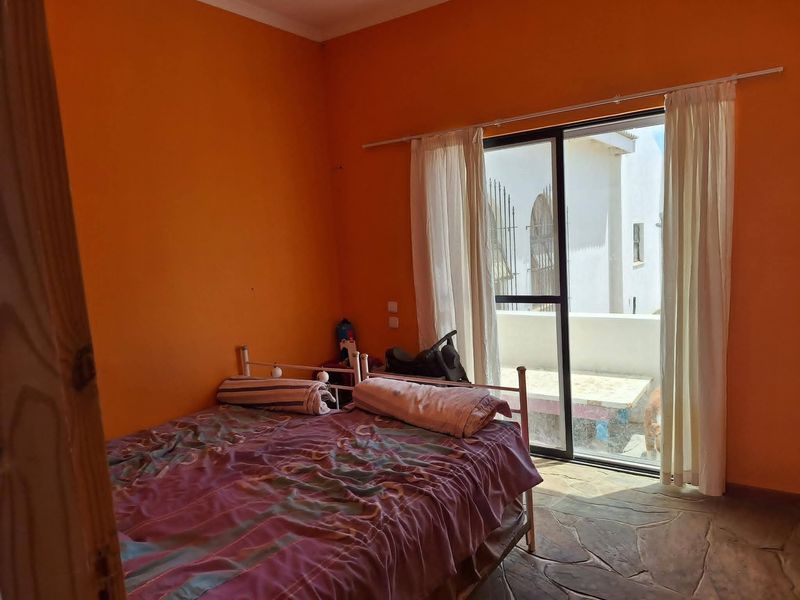 A bedroom featuring stone flooring and a sliding glass door providing access to an outdoor area, with bright orange wall paint.