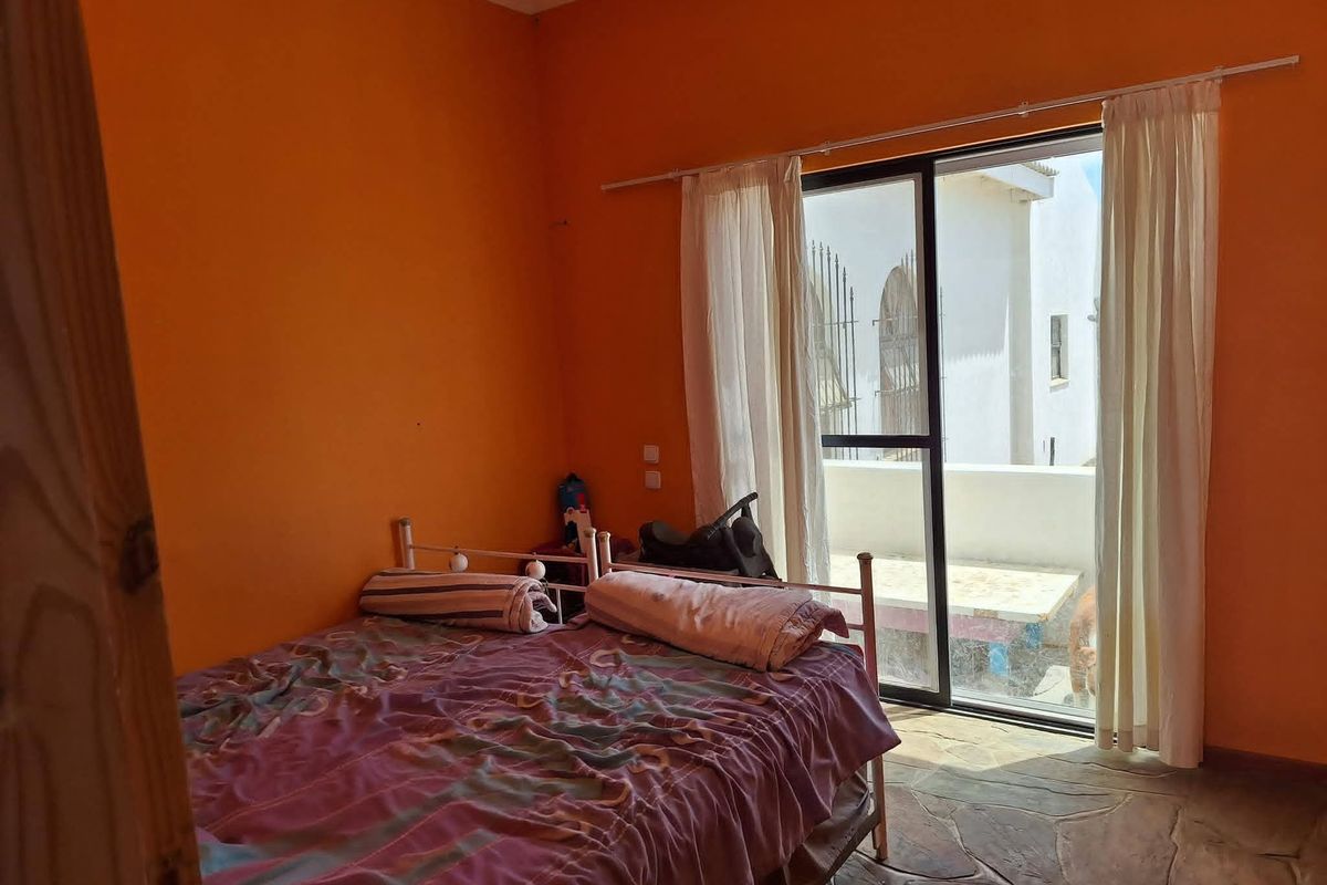A bedroom featuring stone flooring and a sliding glass door providing access to an outdoor area, with bright orange wall paint.