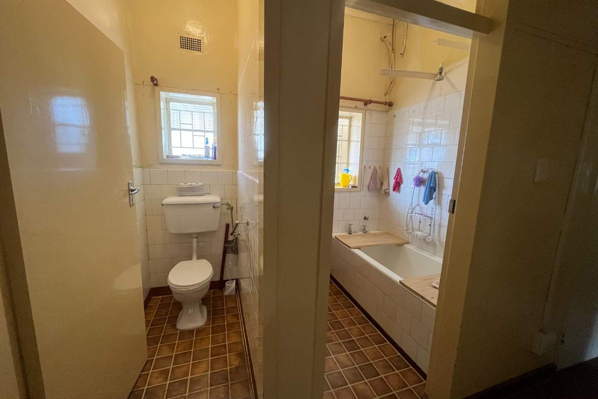 A dated bathroom featuring a separate toilet and a combined bath and shower area with original wall and floor tiling.