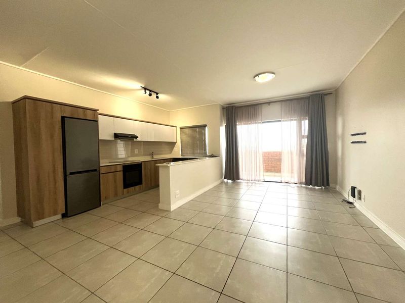 An open-plan living and kitchen area featuring modern cabinetry, built-in appliances, tiled flooring, and a sliding door leading to an outdoor space.