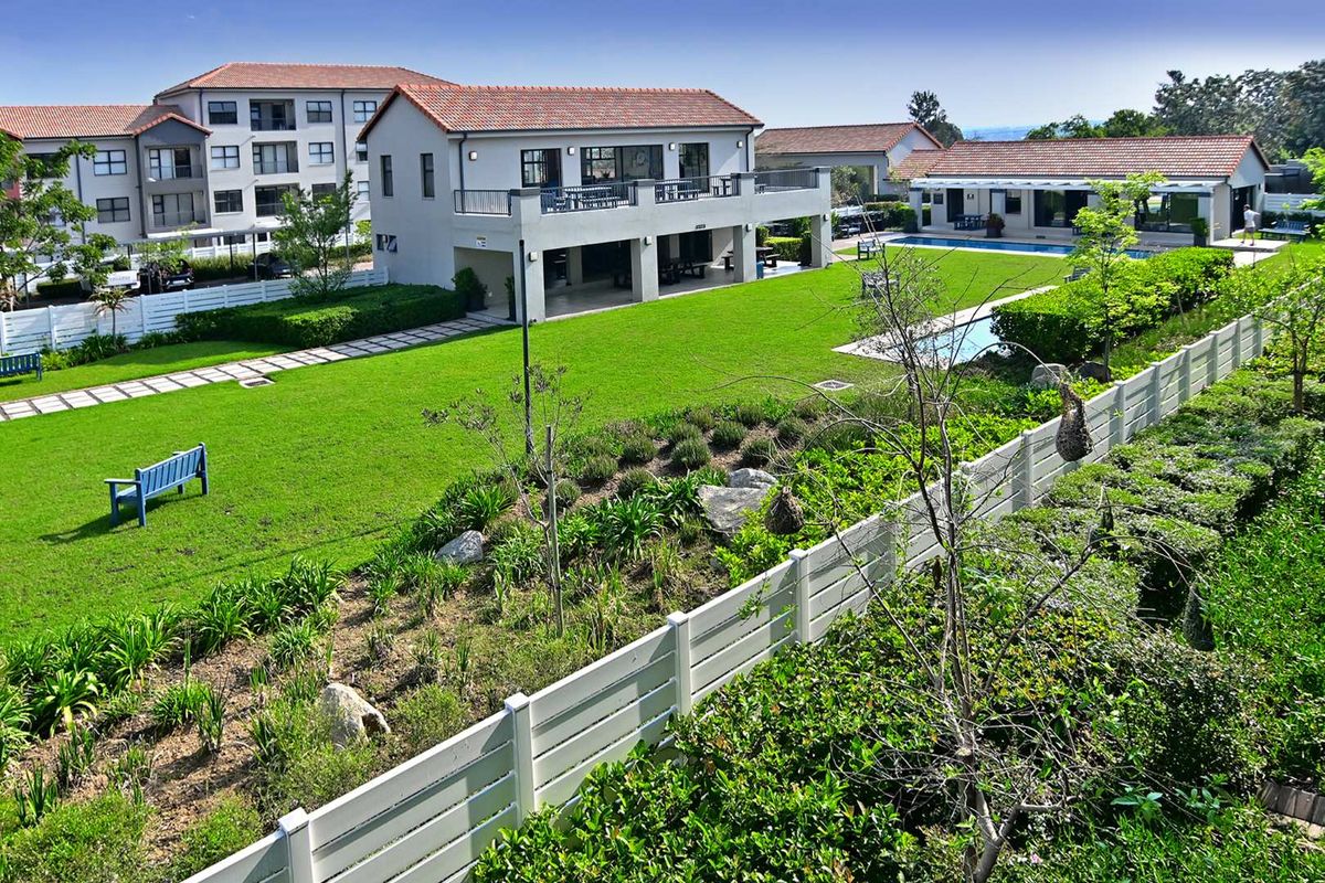 An elevated view of a well-maintained apartment complex featuring a large communal garden, swimming pool, and paved walkways between the residential buildings.