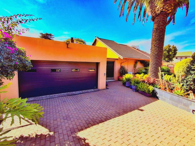 Front elevation of the property featuring a paved driveway, a modern sectional garage door, and a well-maintained landscaped garden area.