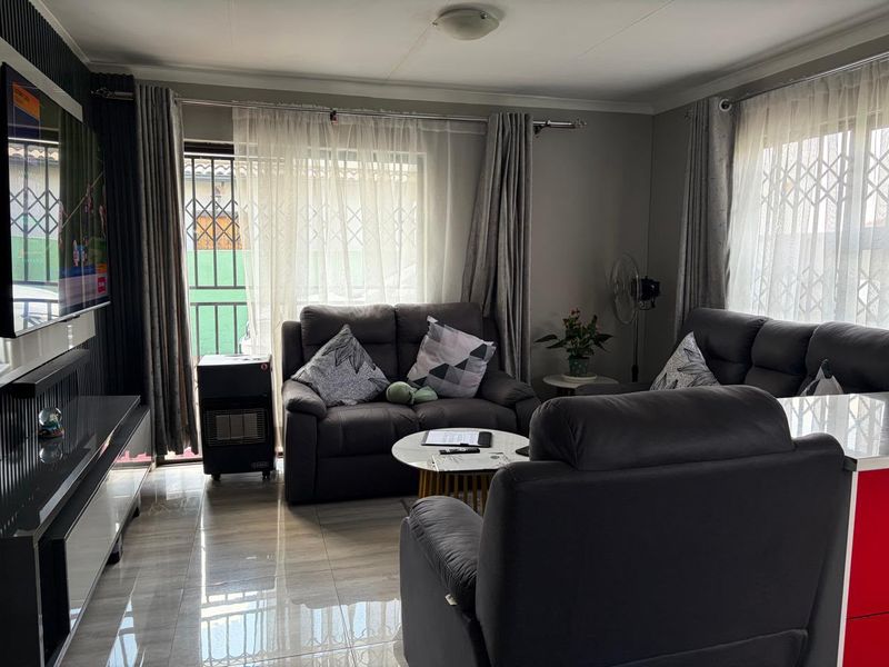 A comfortable living room featuring tiled flooring, large windows with security gates, and sliding door access to the exterior.