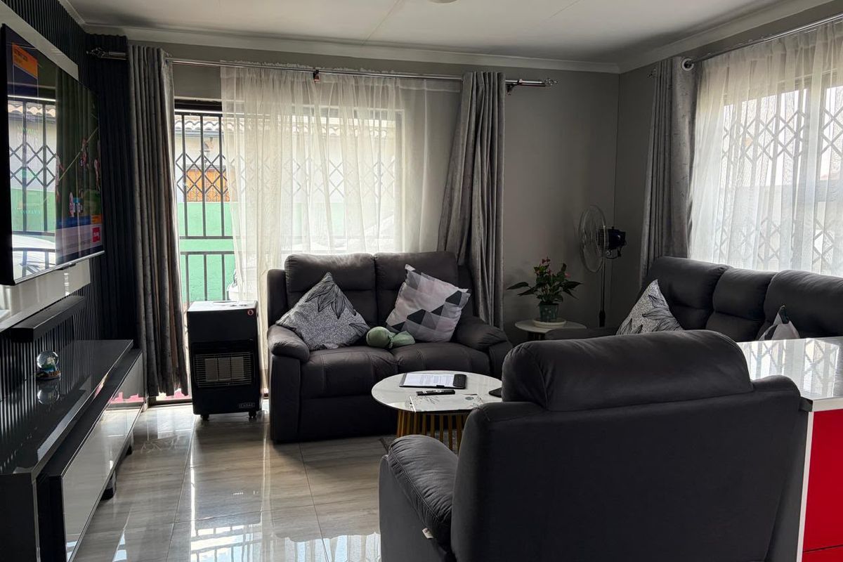 A comfortable living room featuring tiled flooring, large windows with security gates, and sliding door access to the exterior.