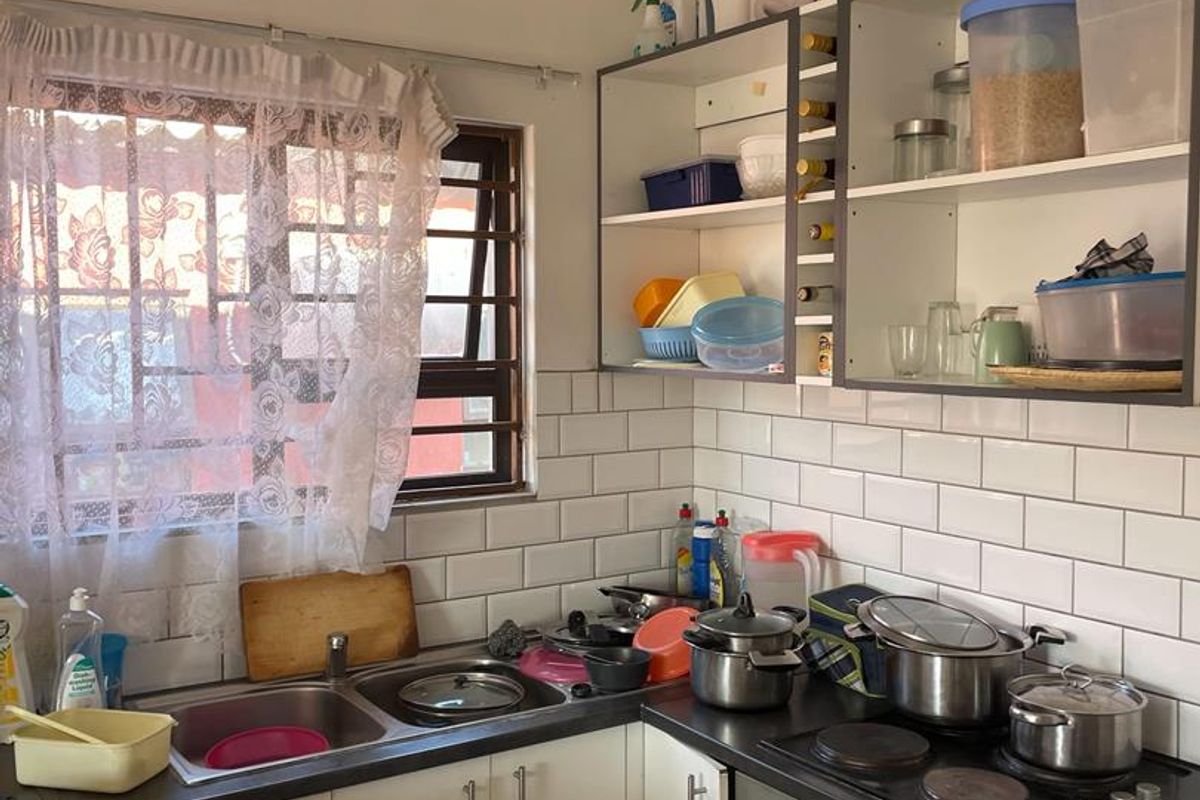 Compact kitchen featuring subway tile backsplash, built-in oven with electric hob, stainless steel sink, and open shelving storage.