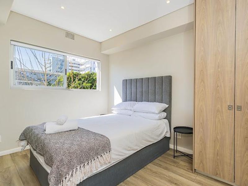 A well-maintained bedroom featuring light wood-look laminate flooring, recessed ceiling lighting, and a built-in wardrobe with a neutral color palette.