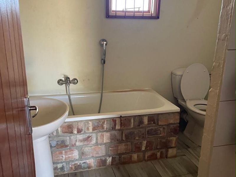 A functional bathroom featuring a pedestal basin, a unique brick-encased bathtub with a handheld shower mixer, and a standard toilet.
