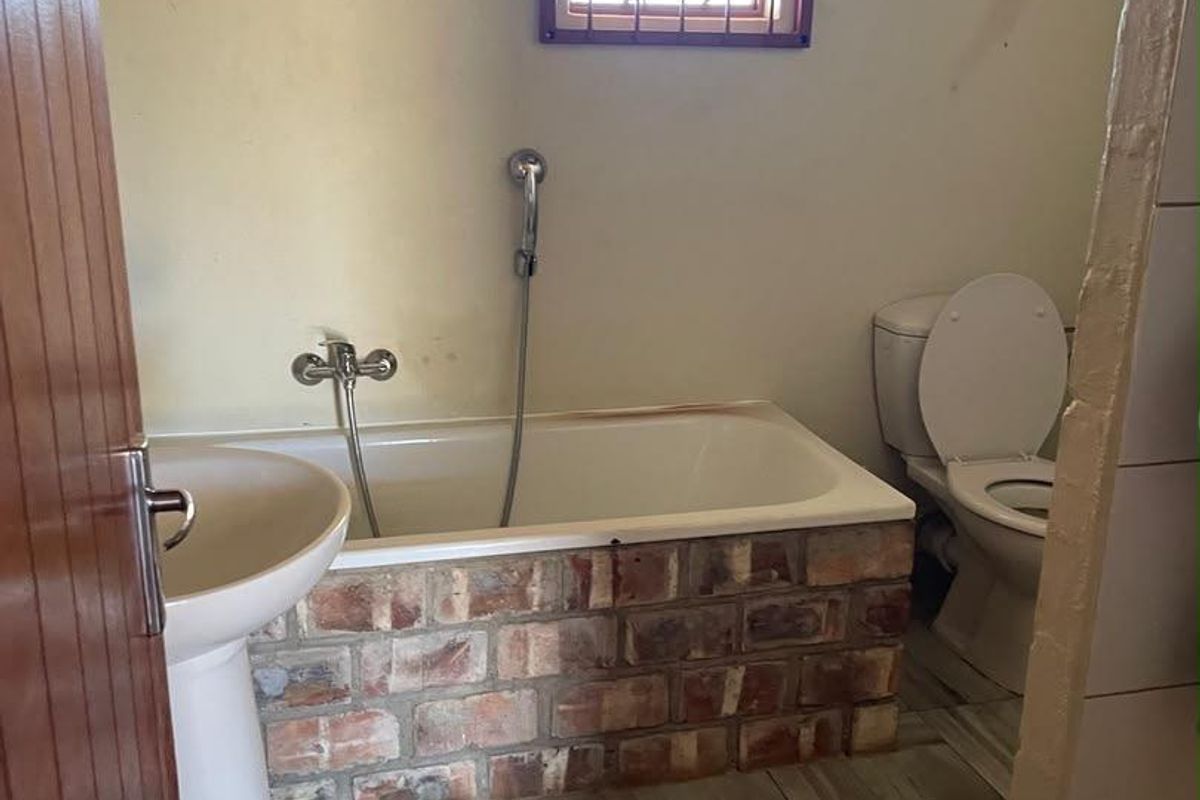 A functional bathroom featuring a pedestal basin, a unique brick-encased bathtub with a handheld shower mixer, and a standard toilet.