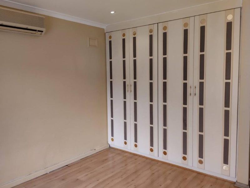 A vacant bedroom featuring laminate flooring, a large built-in wardrobe with decorative panels, and a wall-mounted split-system air conditioning unit.