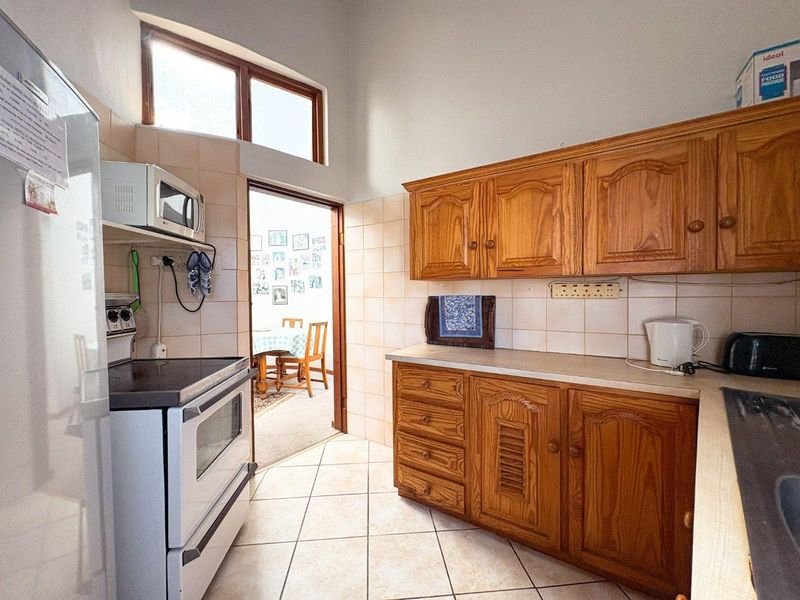 A functional kitchen featuring traditional wooden cabinetry, tiled backsplash, and tiled flooring, offering a classic layout with potential for modern updates.
