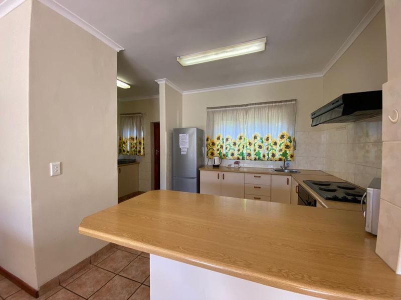 Functional kitchen featuring laminate countertops, built-in cabinetry, electric hob, extractor fan, and tiled backsplash with direct access to a scullery area.