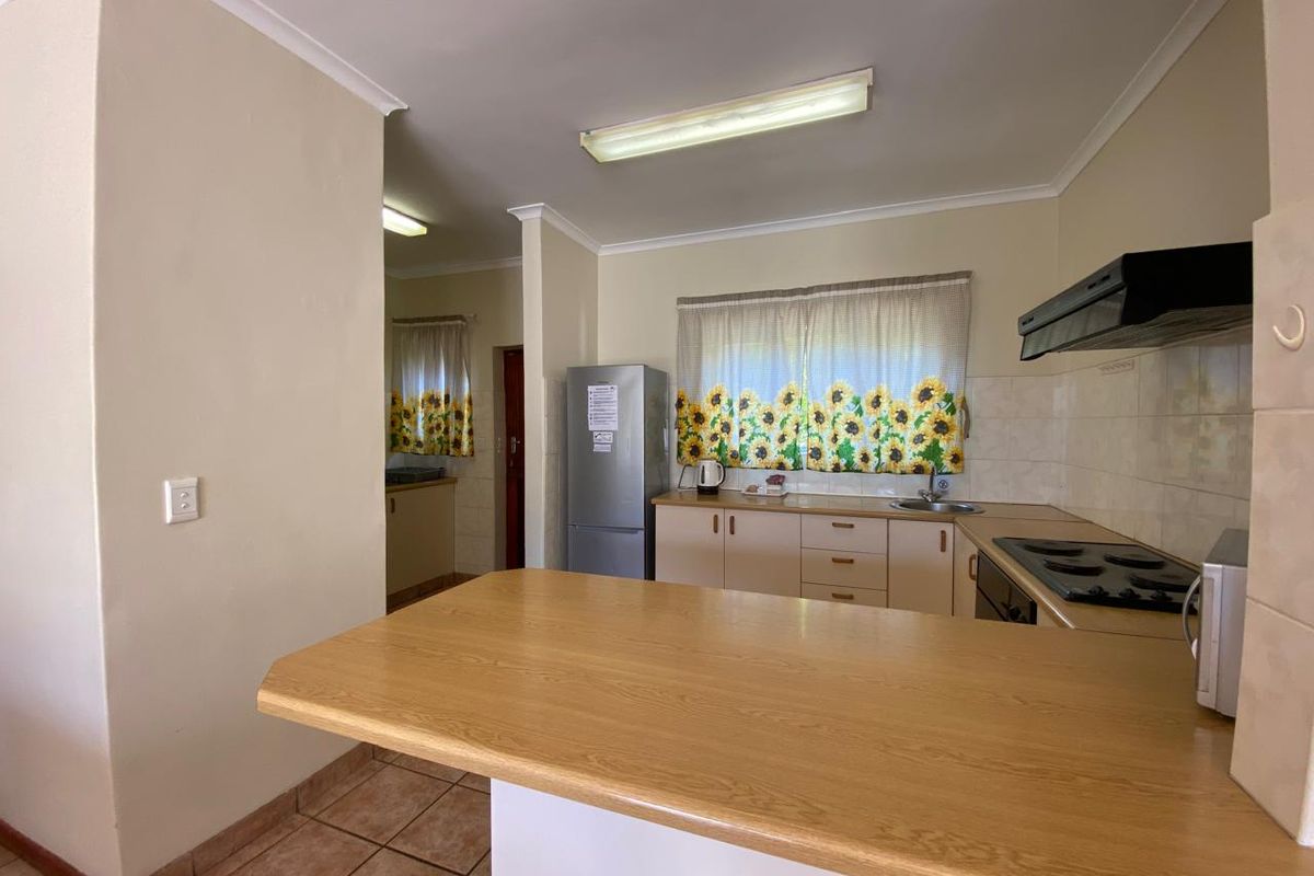 Functional kitchen featuring laminate countertops, built-in cabinetry, electric hob, extractor fan, and tiled backsplash with direct access to a scullery area.